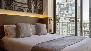 A hotel room with a large bed, a city view, and a decorative wall piece.