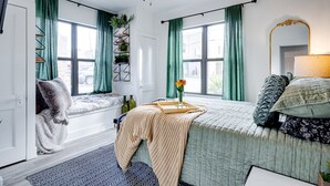 A bedroom with a bed, a window seat, a ceiling fan, and a view of the street.