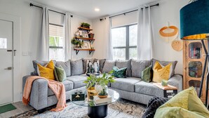A modern living room with a grey sectional sofa, a glass coffee table, and a bookshelf with plants.