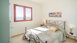 A bedroom with a bed, a nightstand, a lamp, a painting, and a window with a view.