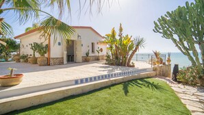 A coastal house with a tiled patio, a lawn, and various plants.