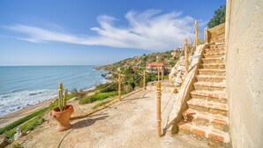 A coastal view with a staircase leading down to the beach, a cactus in a pot, and houses in the background.