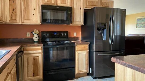 A kitchen with wooden cabinets, a black stove, and a black refrigerator. - Walker's Refuge- large family home, close to river trails (Cody)