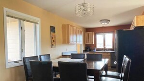 A dining area with a table and chairs, wooden cabinets, and a kitchen in the background. - Walker's Refuge- large family home, close to river trails (Cody)