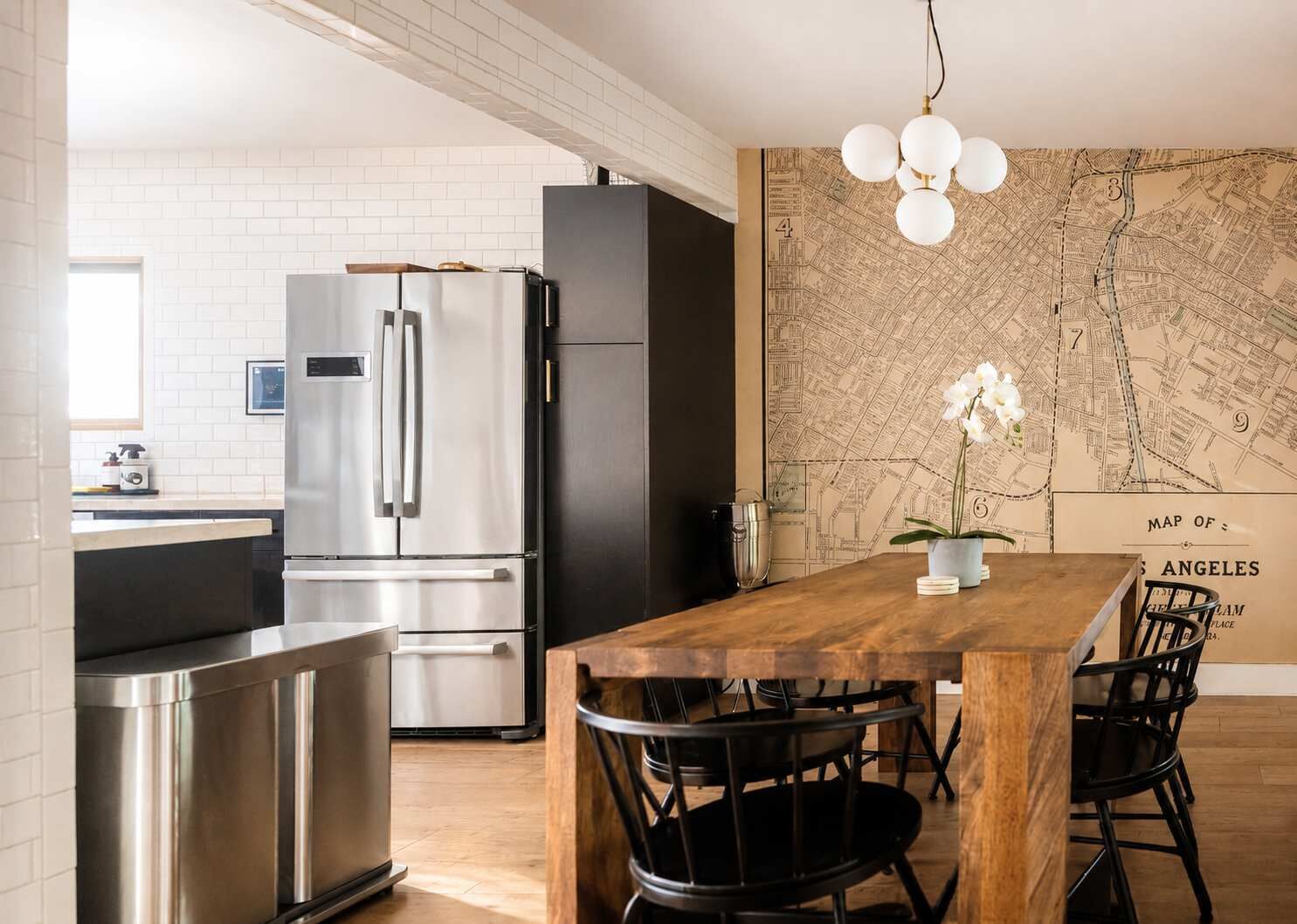 Una cucina moderna con elettrodomestici in acciaio inossidabile, un tavolo da pranzo in legno, sedie nere e una parete con una mappa.