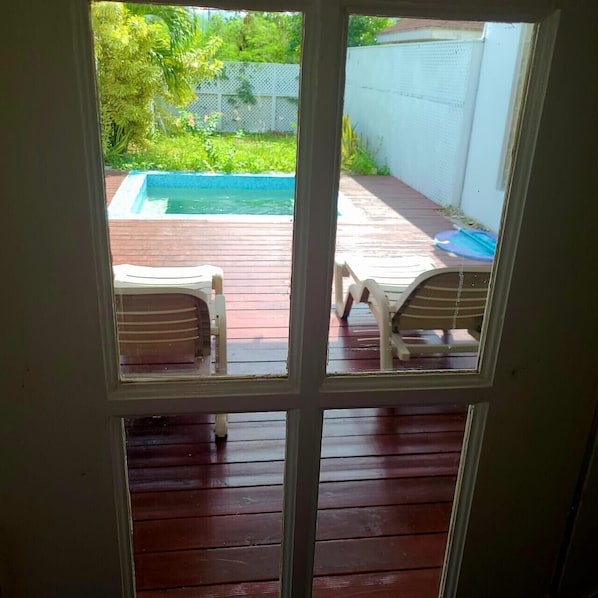 A view through a door to a wooden deck with a pool and two lounge chairs.