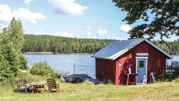 Eine rote Holzhütte mit Tür und Fenstern, einem kleinen Tisch mit Stühlen und einem Boot an der Anlegestelle.