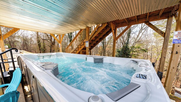 A hot tub with a wooden deck and stairs leading up to it, surrounded by trees. - Lake Front Mountain View w/ 6 King beds (Gainesville)