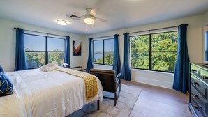 A hotel room with a large bed, a desk, and a view of trees through the windows. - Lake Front Mountain View w/ 6 King beds (Gainesville)
