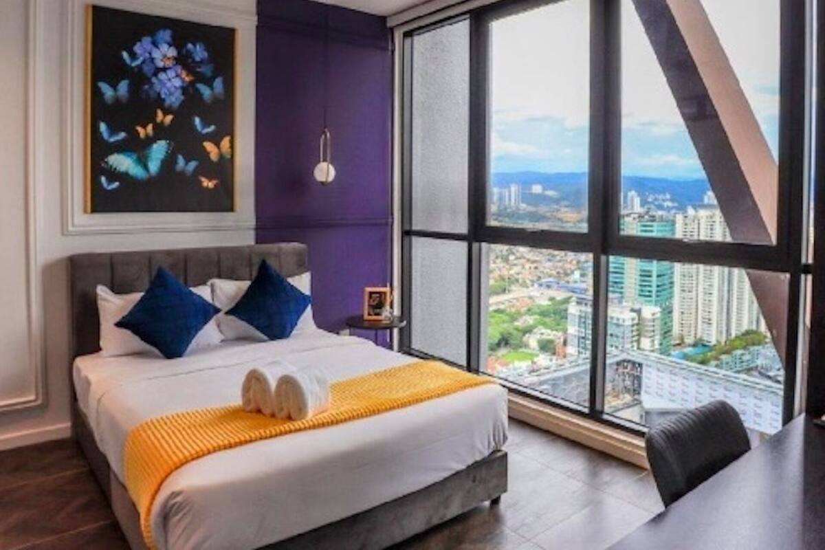 A modern hotel room with a large bed, a city view, and a ceiling fan.