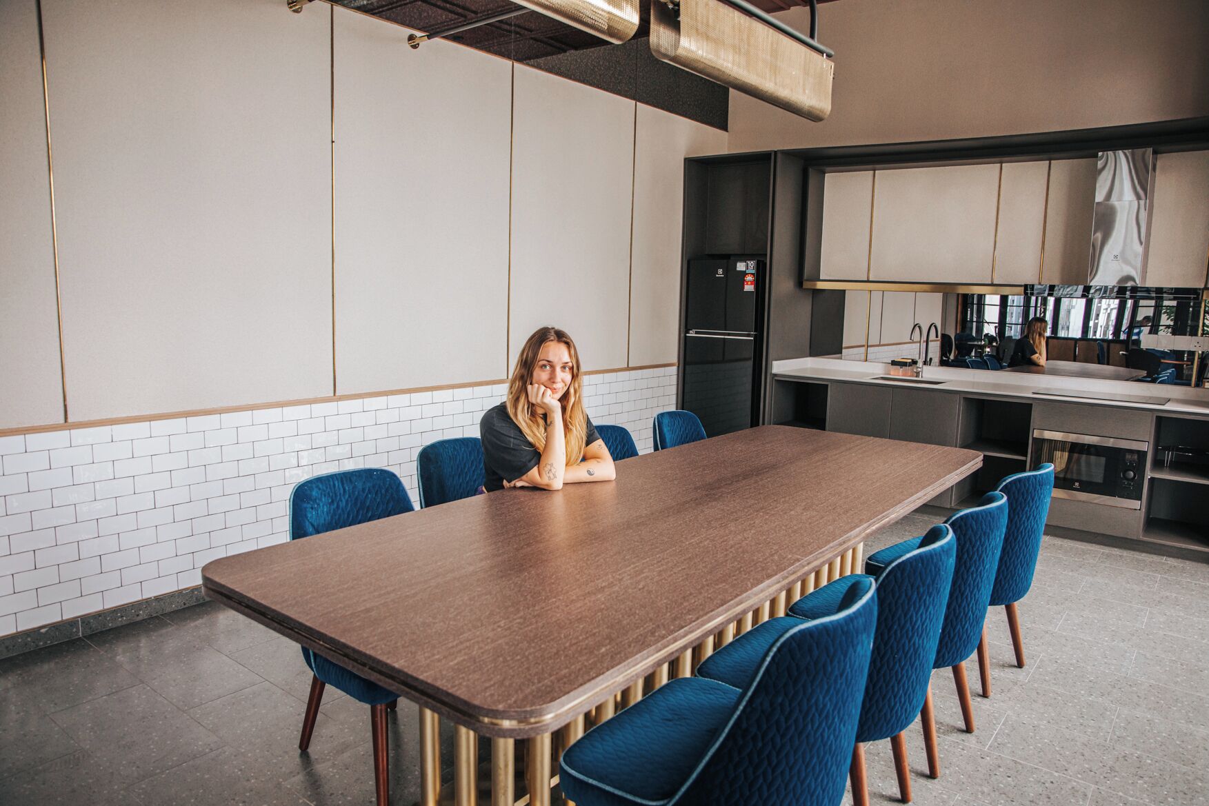 A modern kitchen with a large island, blue chairs, and a person sitting at a table.