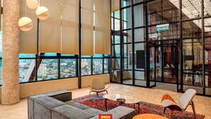 Eine geräumige Lobby mit großzügiger Sitzecke, Blick auf die Stadt durch hohe Fenster und einem modernen Interieur.