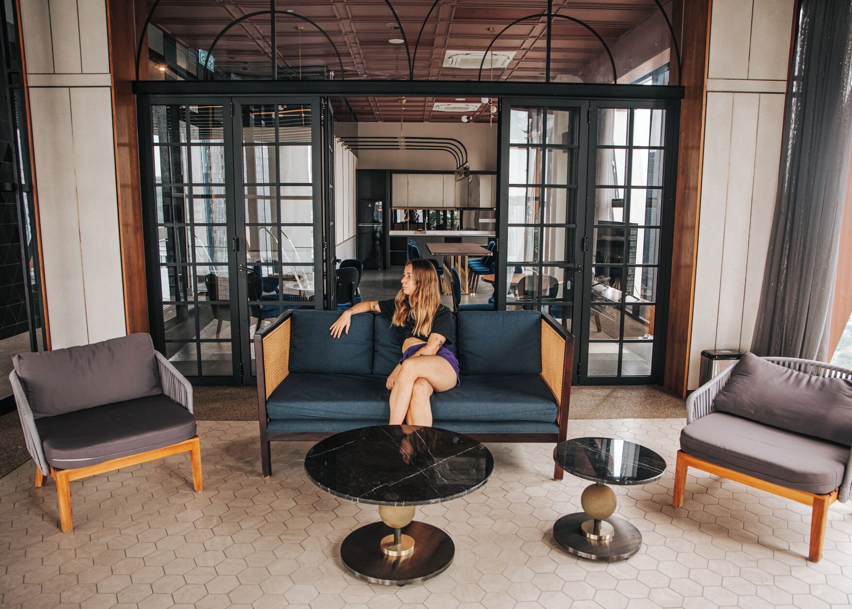 A modern lounge area with a blue sofa, two armchairs, and two round tables.