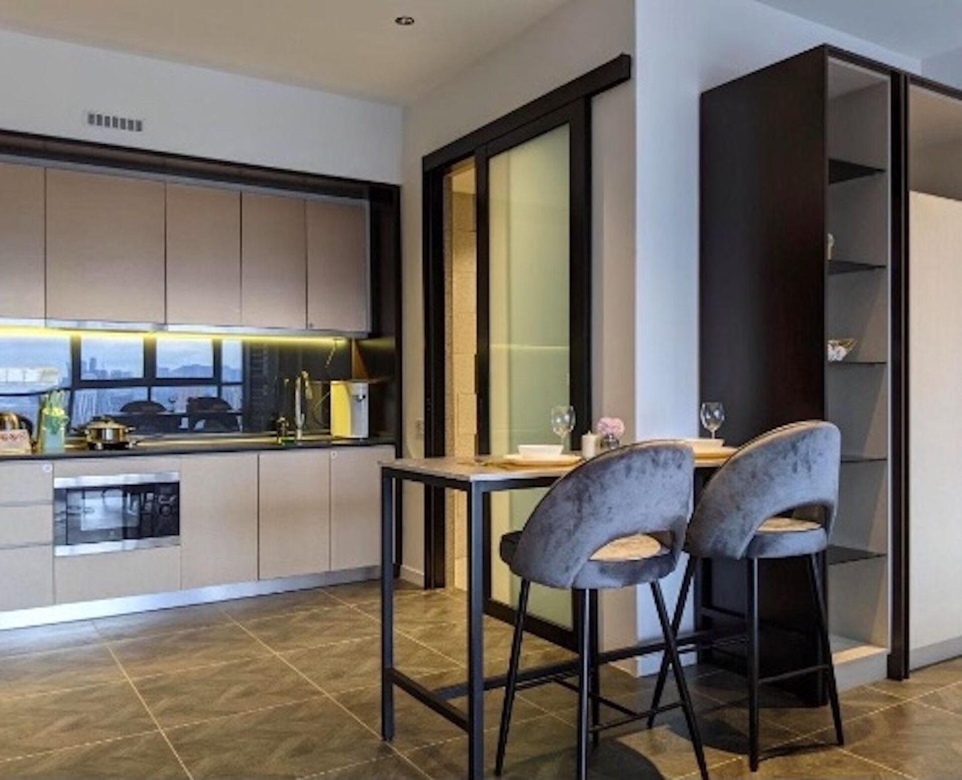 A modern kitchen with a dining area, featuring a large window, a built-in oven, and a dining table with two chairs.