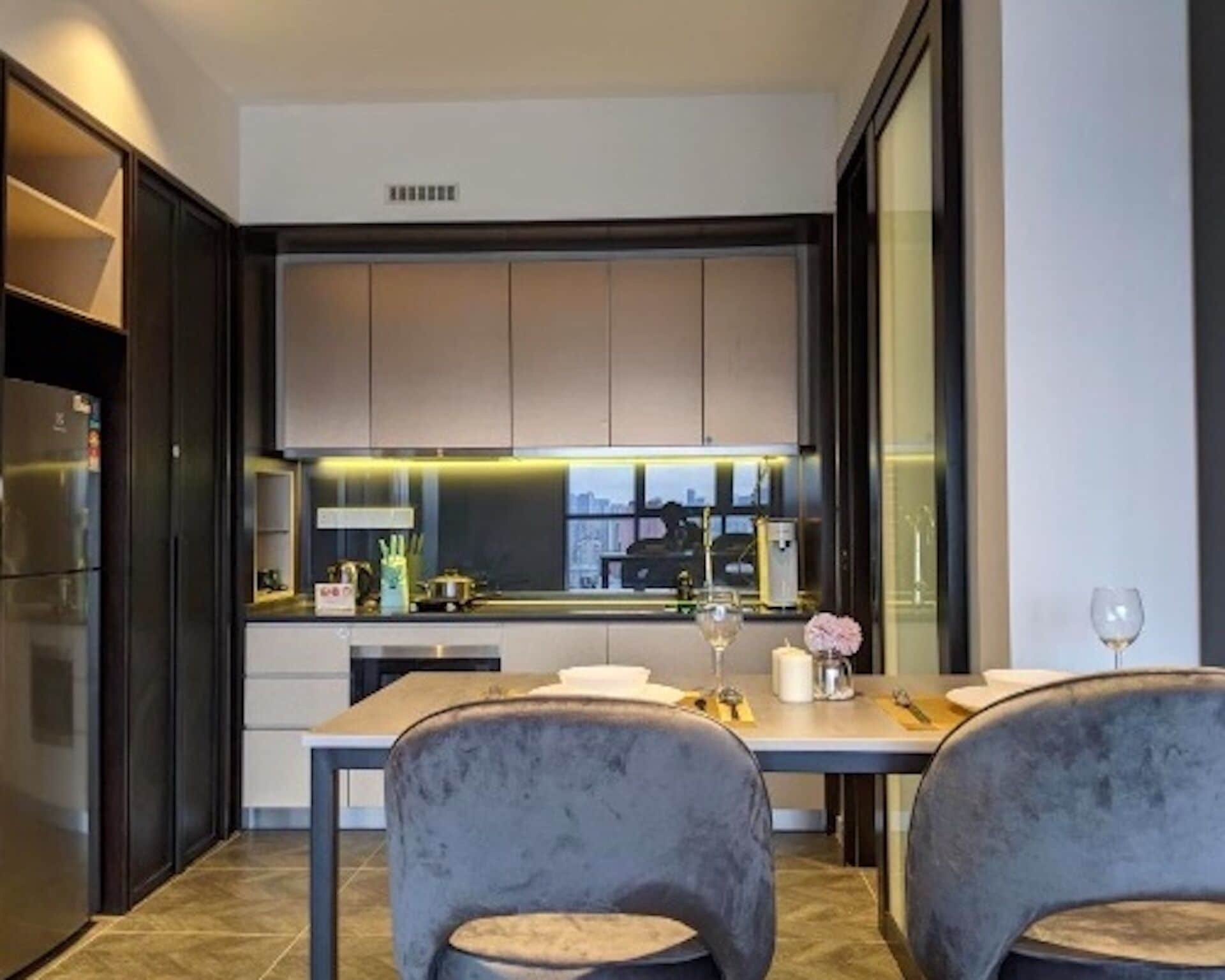 Una cucina moderna con mobili scuri, un'ampia finestra e un'area pranzo con due sedie e un tavolo.