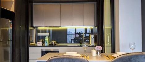 Una cucina moderna con mobili scuri, un'ampia finestra e un'area pranzo con due sedie e un tavolo.