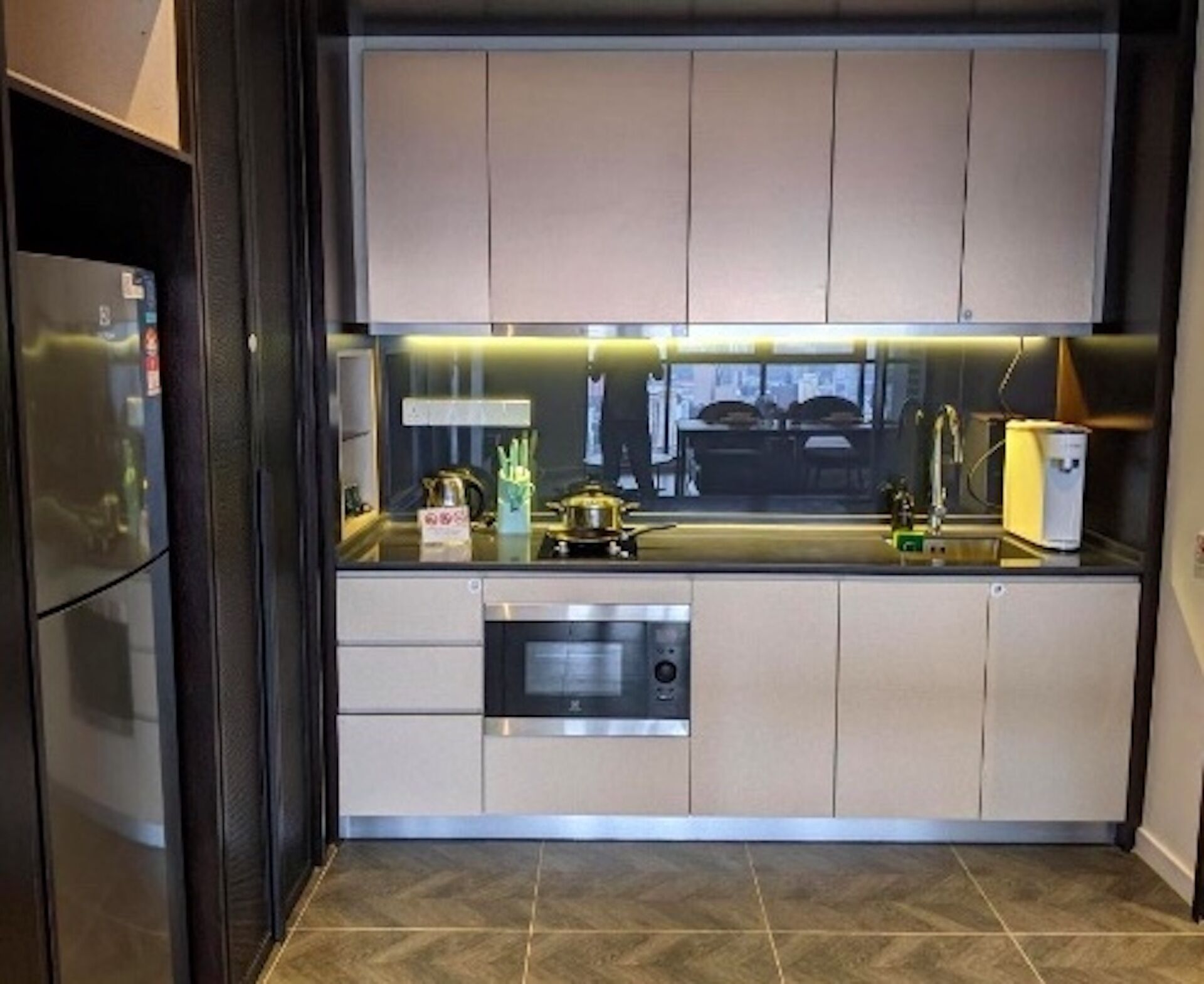 A modern kitchen with a built-in oven, a sink, and a stove. There is a window above the sink, and a refrigerator is visible on the left.