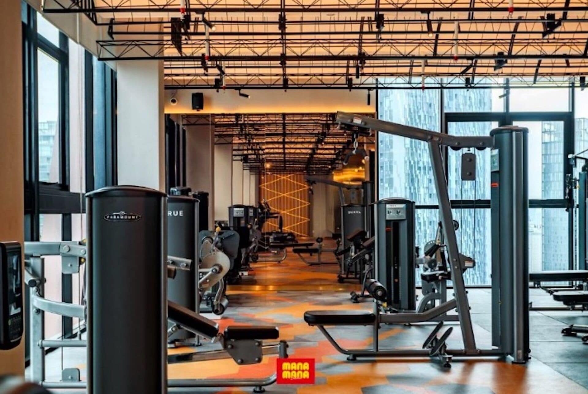 Une salle de sport équipée de divers appareils d’exercice, dotée de grandes fenêtres et d’un plafond haut avec des poutres apparentes.