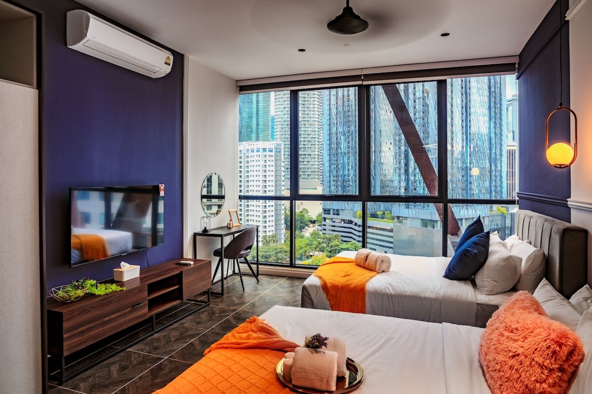 A modern hotel room with two beds, a TV, a desk, and a large window with a city view.