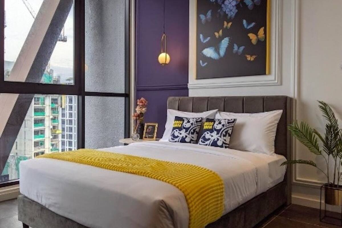 A modern bedroom with a large bed, a view of buildings outside, and a painting of butterflies on the wall.