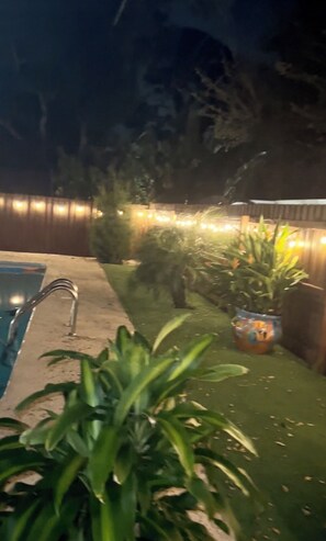 Relax by the pool surrounded by lush greenery and string lights.