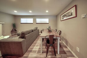 A dining area with a wooden table and chairs, a grey sofa, and a potted plant.