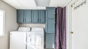 Un cuarto de lavandería con dos lavadoras blancas, armarios color turquesa y una cortina de ducha morada.