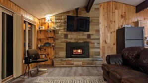A cozy living room with a stone fireplace, wooden walls, a leather couch, and a television mounted above the fireplace. - Moon Lake Waterfront Getaway (Lewiston)