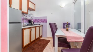 Una cocina compacta con refrigerador, cafetera y una mesa de comedor con sillas moradas.
