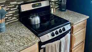 Een keuken met houten kastjes, een roestvrijstalen magnetron, een zwart fornuis en een granieten aanrecht.
