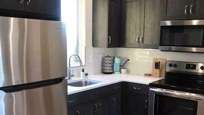 A modern kitchen with dark cabinets, stainless steel appliances, and a wooden floor. - Private Scenic Stay at Sycamore Lane (Hurricane)