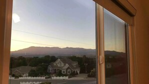 A view through a window of a residential street with houses, a white picket fence, and mountains in the background. - Private Scenic Stay at Sycamore Lane (Hurricane)