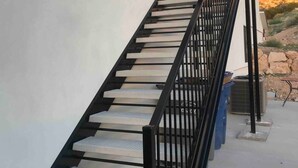 A staircase with black railings leading to a door, set against a white wall with a view of a rocky landscape. - Private Scenic Stay at Sycamore Lane (Hurricane)