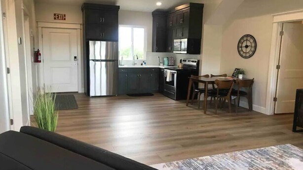 A modern kitchen with dark cabinets, a dining area with a table and chairs, and a visible exit sign. - Private Scenic Stay at Sycamore Lane (Hurricane)