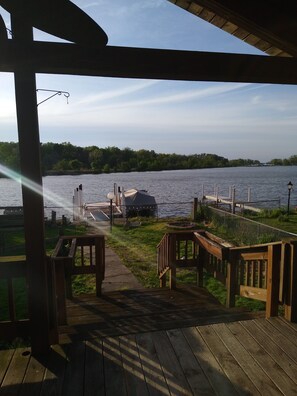 Une terrasse en bois avec vue sur un lac, un barbecue et un kiosque.