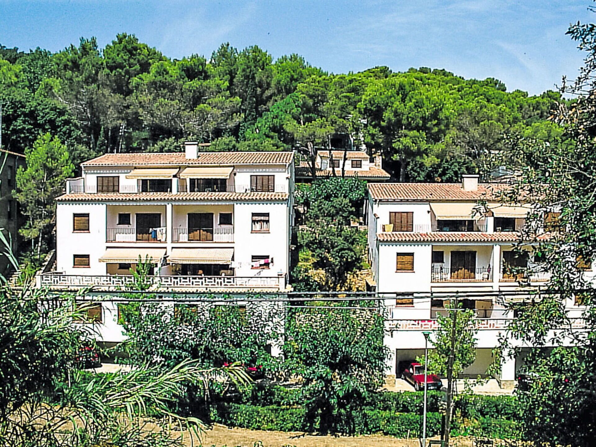 A two-story residential building with a tiled roof, balconies, and a garden area.