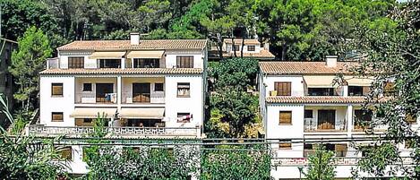A two-story residential building with a tiled roof, balconies, and a garden area.