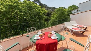 A rooftop terrace with a table set for four, surrounded by green chairs and white lounge chairs.