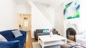 A modern living room with a staircase, a fireplace, and a large abstract painting. - Entire 4 Bedroom Paddington Terrace (Paddington)