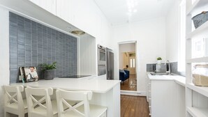 A modern kitchen with white cabinetry, a central island with seating, and a view into the adjacent living area. - Entire 4 Bedroom Paddington Terrace (Paddington)