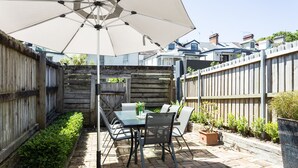 A patio area with a table and chairs, a large umbrella, and a wooden fence. - Entire 4 Bedroom Paddington Terrace (Paddington)