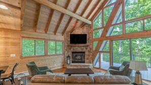 Ein gemütliches Blockhaus-Interieur mit Kamin aus Stein, Holzbalken, großen Fenstern und Ledersitzmöbeln.