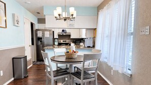 A dining area with a round table, white chairs, a chandelier, and a kitchen in the background. - Cheerful Home w/ Private Hot Tub, Big Fenced Yard, & Pool.  Pet Friendly! (Crowley)