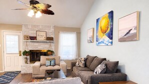 A living room with a fireplace, a sofa, a coffee table, and artwork on the wall. - Cheerful Home w/ Private Hot Tub, Big Fenced Yard, & Pool.  Pet Friendly! (Crowley)