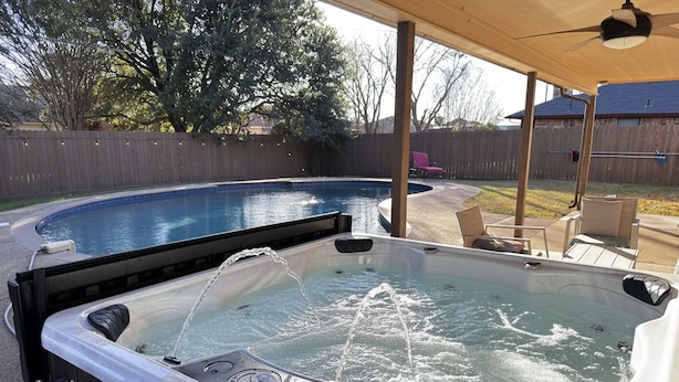 A hot tub with water jets, a pool, and outdoor furniture under a covered area. - Cheerful Home w/ Private Hot Tub, Big Fenced Yard, & Pool.  Pet Friendly! (Crowley)
