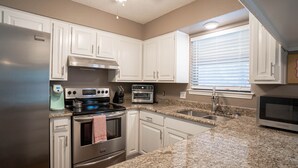 A kitchen with white cabinets, stainless steel appliances, granite countertops, and a window with blinds. - Cheerful Home w/ Private Hot Tub, Big Fenced Yard, & Pool.  Pet Friendly! (Crowley)