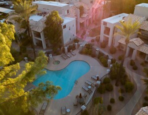 An aerial view of a resort with a swimming pool surrounded by lounge chairs and palm trees.