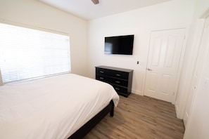 Une chambre à coucher avec un lit, une commode, un téléviseur et une porte.