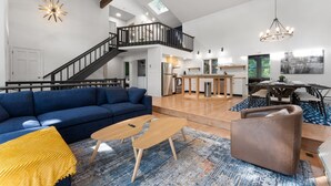 Un salon spacieux avec un canapé bleu, une table basse en bois et un fauteuil marron. Un escalier mène à l’étage supérieur.