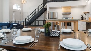 Un coin repas avec une table en bois dressée pour le repas, un escalier et une cuisine en arrière-plan.